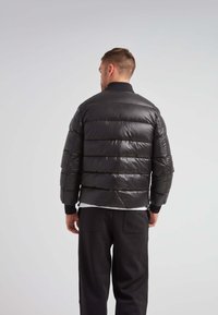 Giubbotto imbottito nero con design a quadri orizzontali, polsini elasticizzati e colletto alla coreana. Presenta una texture lucida e liscia e una chiusura con zip.