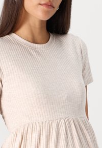 Ljus beige klänning med ribbad struktur, korta ärmar, rund halsringning och samlad midja för en flödande silhuett.