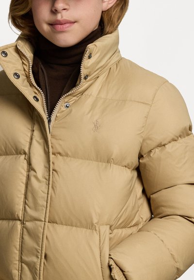 Beige pufferjakke med høy krage, trykknapper og brodert logo på venstre bryst. Glatt tekstur med quiltede seksjoner.