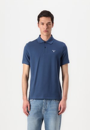 Navyblauwe polo gemaakt van katoen, met een klassieke kraag, korte mouwen en een geborduurd logo op de borst. Gecombineerd met lichtblauwe jeans.