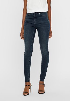 Σκούρα μπλε skinny jeans από τζιν, με ψηλή μέση και λεία υφή. Συνδυασμένα με μαύρες strappy ψηλές γόβες.