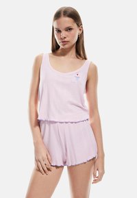 Conjunto de pijama en dos piezas de color rosa claro, hecho de tela acanalada. La parte superior tiene un escote en forma de barco y un pequeño diseño bordado; los pantalones cortos tienen un dobladillo con volantes.