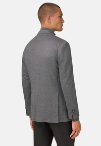 Šedý texturovaný blazer s jemným herringbone vzorem, s klopovým límcem, s jedním rozštěpem na zadní straně a na knoflíkové manžety.