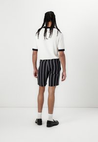 White short-sleeve sweater with navy trim, paired with navy striped shorts and black shoes. Model is turned away, showcasing the back view.