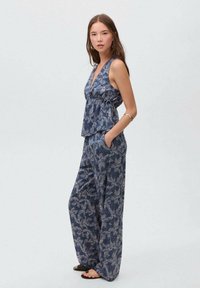 Tyrkysově modrý dvoudílný outfit s květinovým vzorem, který se skládá z topu bez rukávů s peplum a širokých kalhot, vyrobený z lehkého materiálu.