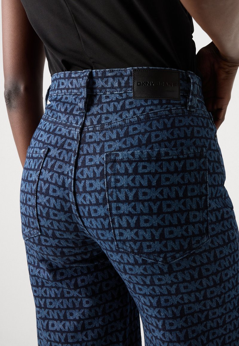 Jeans de mezclilla con un estampado azul y el logo repetido de "DKNY". Diseño de cintura alta con una superficie texturizada y bolsillos traseros. Etiqueta negra en la cinturilla.
