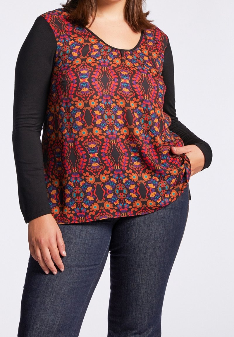 Multicolor long-sleeve top featuring a black base, floral pattern in red, orange, and blue, with a scoop neckline and relaxed fit. Denim jeans are worn.