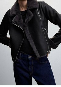 Czarna skórzana kurtka z szarym kołnierzem i mankietami z baranka, z ukośnym zamkiem błyskawicznym i klasycznym krojem, zestawiona z ciemnymi dżinsami.