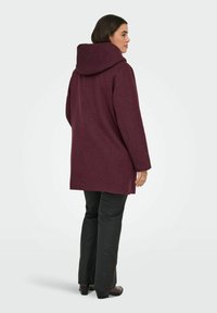 Vínová vlněná bunda s kapucí, dlouhými rukávy a rovný střih. Hladká textura, minimalistický design a délka do poloviny stehna.