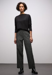 Zwarte gebreide trui met opgerolde halslijn gecombineerd met hooggetailleerde geruite broek met zijknopen, gedragen met robuuste zwarte laarzen.