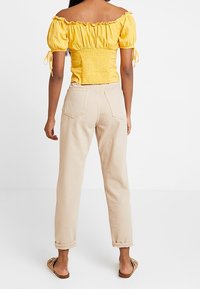 Top giallo senza spalline con corpetto arricciato e maniche a sbuffo, abbinato a pantaloni beige a vita alta e sandali piatti marroni.