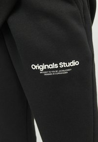 Schwarzer Baumwollpullover mit dem Text "Originals Studio" in Weiß, mit glatter Textur und minimalistisches Design.