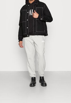 Sort denimjakke med hvid syning over en sort hoodie, parret med lysegrå sweats, der har logo, og sorte ankelstøvler.
