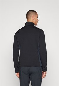 Felpa nera con zip e colletto alto, in tessuto strutturato, con pannelli laterali a contrasto. Design semplice e aderente senza decorazioni.