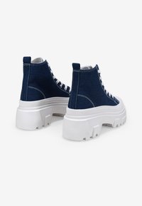 Zapatillas altas de mezclilla azul marino con cordones blancos y una suela gruesa de goma blanca. Las características incluyen costuras en contraste y una superficie texturada.