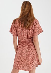 Šaty s krátkým rukávem v růžové tkanině s tečkovaným vzorem v černé a bílé. Mají elastický pas a volný střih.