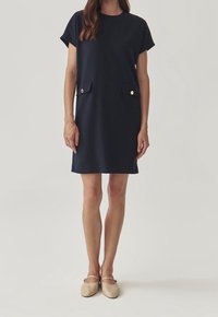 Navy blue short-sleeve shift dress with a round neckline, two front pockets, and gold button accents. Smooth texture, above-knee length.