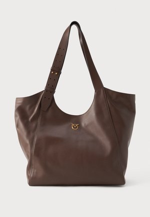 Saco tote de couro castanho com uma textura suave, apresentando um emblema dourado na parte da frente e uma alça ajustável com furos para ajuste de comprimento.