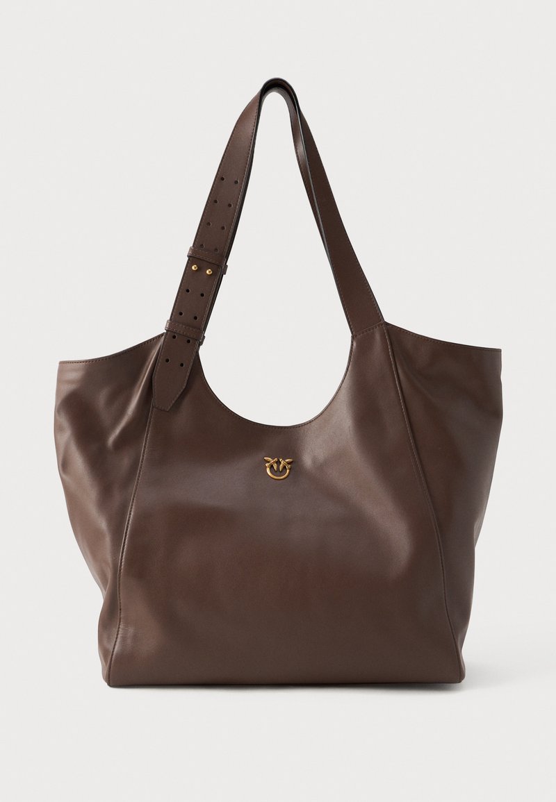 Saco tote de couro castanho com uma textura suave, apresentando um emblema dourado na parte da frente e uma alça ajustável com furos para ajuste de comprimento.