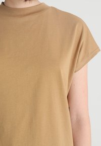 Top marrón de manga corta con un cuello alto, hecho de una tela suave, que presenta un corte relajado y un detalle de costura mínima en las mangas.