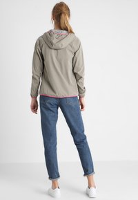 Lichtgrijze, capuchonjack met elastische manchetten, roze accenten en een licht getailleerd ontwerp, gecombineerd met blauwe jeans en witte schoenen.