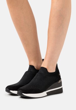 Černé slip-on tenisky s texturovaným svrškem, které mají jemný lesk, platformu a bílé akcenty na podešvi. Hladká tkanina a elastický lem.