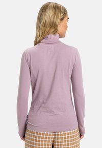 Maglione a collo alto a maniche lunghe color lilla con una consistenza morbida, design aderente, cuciture piatte e un colletto sottile. Indossato con pantaloni a fantasia scozzese.
