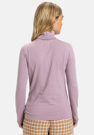 Maglione a collo alto a maniche lunghe color lilla con una consistenza morbida, design aderente, cuciture piatte e un colletto sottile. Indossato con pantaloni a fantasia scozzese.