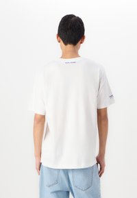 T-shirt en coton blanc à manches courtes, arborant un logo bleu "PEPE JEANS" dans le dos et un branding discret sur la manche gauche.