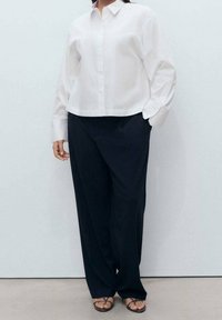 Chemise blanche à col, associée à un pantalon noir ample et des sandales à brides, présentant un design uni et une texture de tissu lisse.