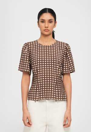 Brown and cream checked short-sleeve top with a round neckline and gathered shoulders, paired with light-colored pants.