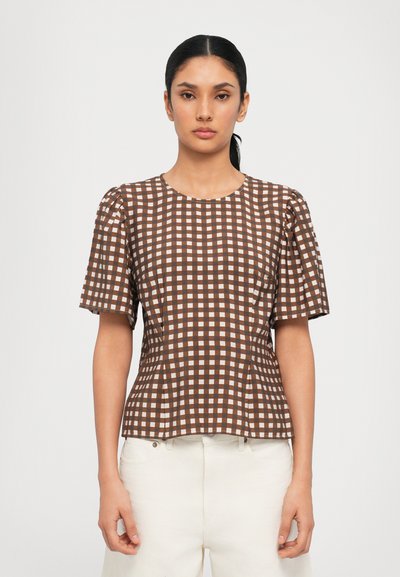 Bruin en crème geruite kortgelehem shirt met een ronde halslijn en geplooide schouders, gecombineerd met lichtgekleurde broek.