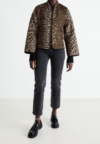 Gewatteerde jas met luipaardprint en brede mouwen, zwarte biezen, gedragen over zwarte spijkerbroeken en glanzende plateauzolen. Gestructureerd en opvallend ontwerp.