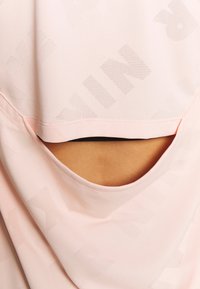 Ljust rosa träningslinne med rundad halsringning, öppen ryggdetalj och subtilt strukturerat mönster av varumärket. Mjuk, ventilerande tyg.