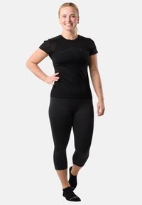 Black athletic top with short sleeves, featuring a mountain design; paired with black ¾ leggings. Model wears black socks.