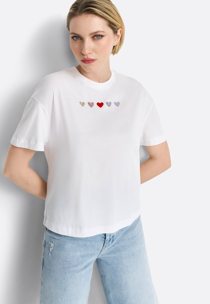 White short-sleeve t-shirt featuring five embroidered hearts in gold, red, and blue. The shirt has a relaxed fit and a round neckline.