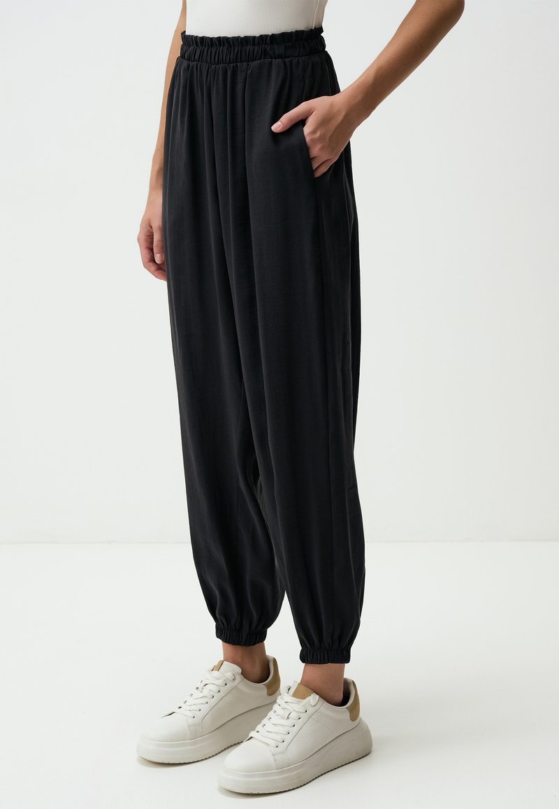 Pantaloni neri, morbidi e ampi, con una cintura elastica e tasche laterali, che si restringono alla caviglia, abbinati a sneakers bianche.