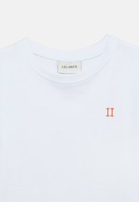 Άσπρο βαμβακερό t-shirt με στρογγυλή λαιμόκοψη και μικρή πορτοκαλί κεντημένη επιγραφή "II" στην αριστερή πλευρά. Μινιμαλιστικός σχεδιασμός και λεία υφή.