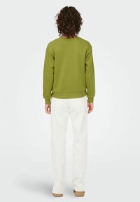 Olivově zelená mikina z měkké látky s kulatým výstřihem, žebrovanými manžetami a volným střihem, doplněná o bílé kalhoty s širokými nohavicemi.