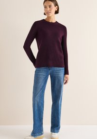 Bordeaux geribbelde gebreide trui met lange mouwen, gecombineerd met lichtblauwe wijde jeans en witte sneakers met beige accenten.