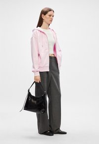 Svetlo ružová zipsová mikina, biele crop top, šedé široké nohavice s prúžkami, čierna kožená taška na rameno a čierne nazúvacie topánky.