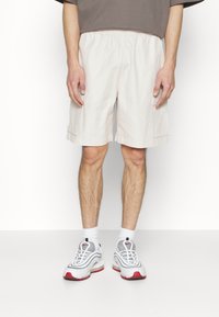 Beige šortky s elastickým pasem, cargo kapsami a volným střihem, doplněné o šedé a červené sportovní boty a bílé kotníkové ponožky.