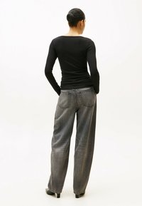 Top nero a maniche lunghe aderente, abbinato a jeans grigi in denim larghi, con taglio dritto, leggere sfumature e tasche posteriori.