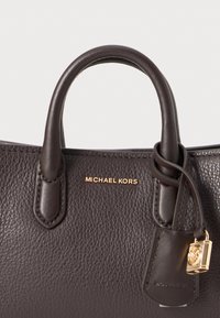 Dunkelbraune Lederhandtasche mit strukturiertem Design, zwei Griffen, goldenen Beschlägen und einem kleinen Schlossakzent. Graviertes "Michael Kors"-Logo sichtbar.