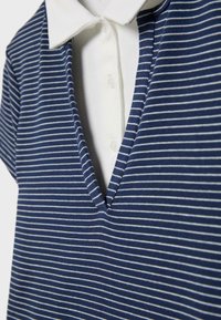 Gros plan sur un vêtement à col en V rayé bleu marine et blanc, superposé à une chemise blanche à col boutonné.