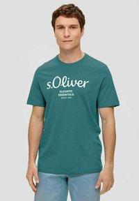 Türkisblaue Baumwoll-T-Shirt mit kurzen Ärmeln und rundem Halsausschnitt. Auf der Vorderseite befindet sich der weiße Text "s.Oliver Elevated Essentials Since 1969".