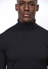 Schwarzer Rollkragenpullover aus geripptem Stoff, taillierter Schnitt, mit hohem Kragen und nahtloser Konstruktion, die eine glatte Textur zeigt.