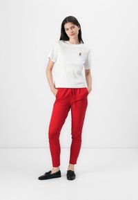 T-shirt en coton blanc à manches courtes avec un logo d'ours, associé à des joggeurs rouges à taille élastique. Des chaussures noires à semelles plates complètent la tenue.