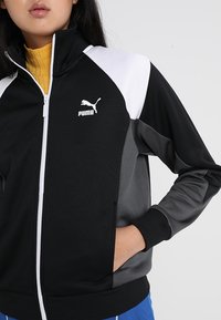 Svart och grå zip-up jacka med vita detaljer och Puma-logga, med hög krage, ribbade ärmslut och sidofickor. Strukturerad tyg.