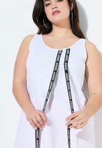 Abito tank bianco con scollatura a coppia, dotato di spalline nere con la scritta "ANGEL" disposta verticalmente sulla parte anteriore. Tessuto dalla texture liscia.